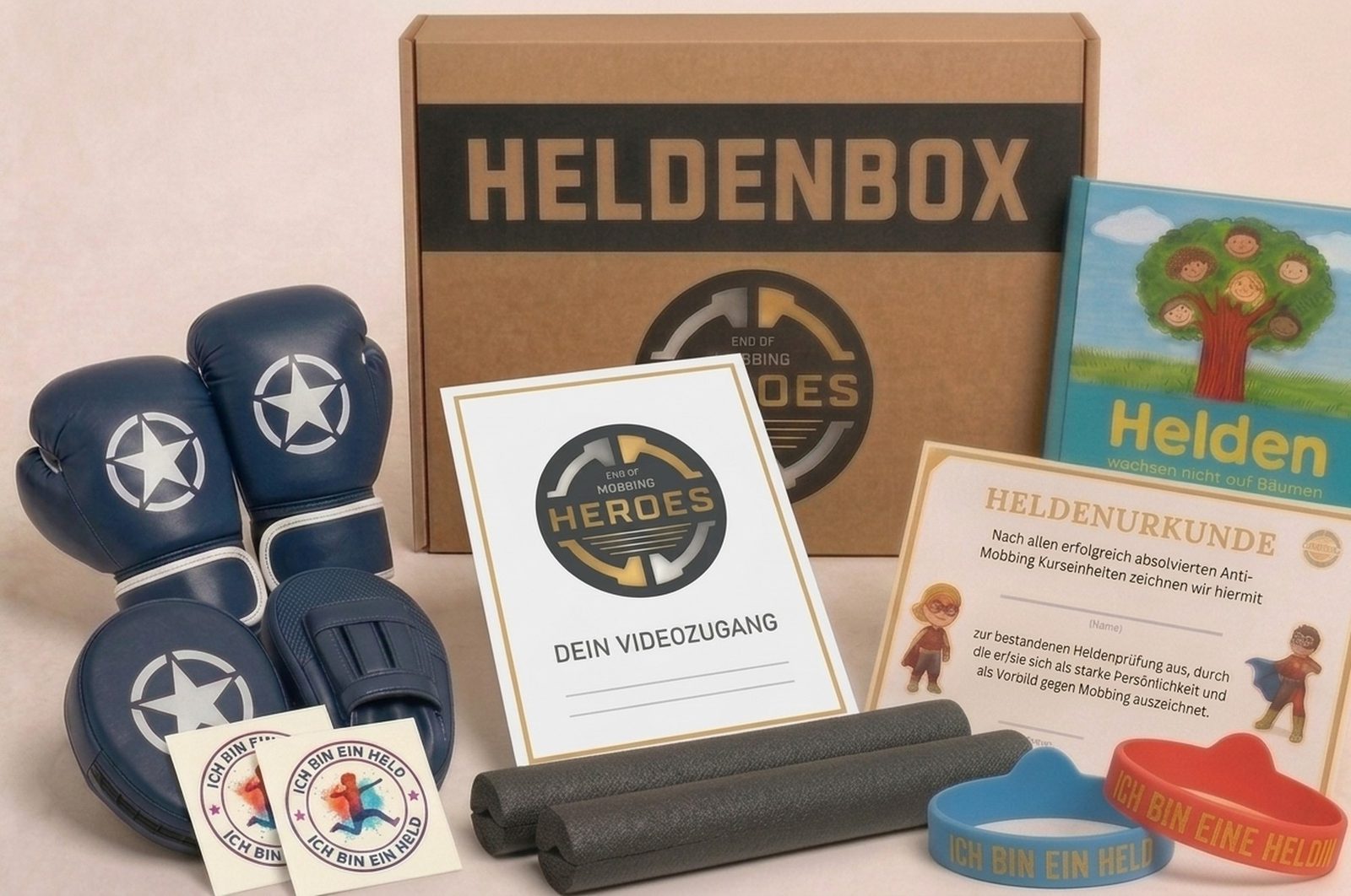 Die echte Heldenbox: Naturkarton mit HELDENBOX-Schriftzug und EOM-Logo, davor Boxhandschuhe, Pratzen, zwei Trainingssticks, Heldenbuch, Urkunde, Heldenarmbänder, Tattoos und die Karte für den Videozugang