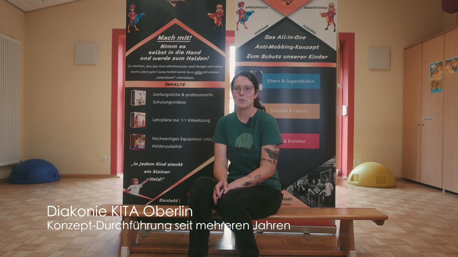 Erzieherin der Diakonie-Kita Oberlin sitzt vor zwei Aufstellern von EOM Heroes