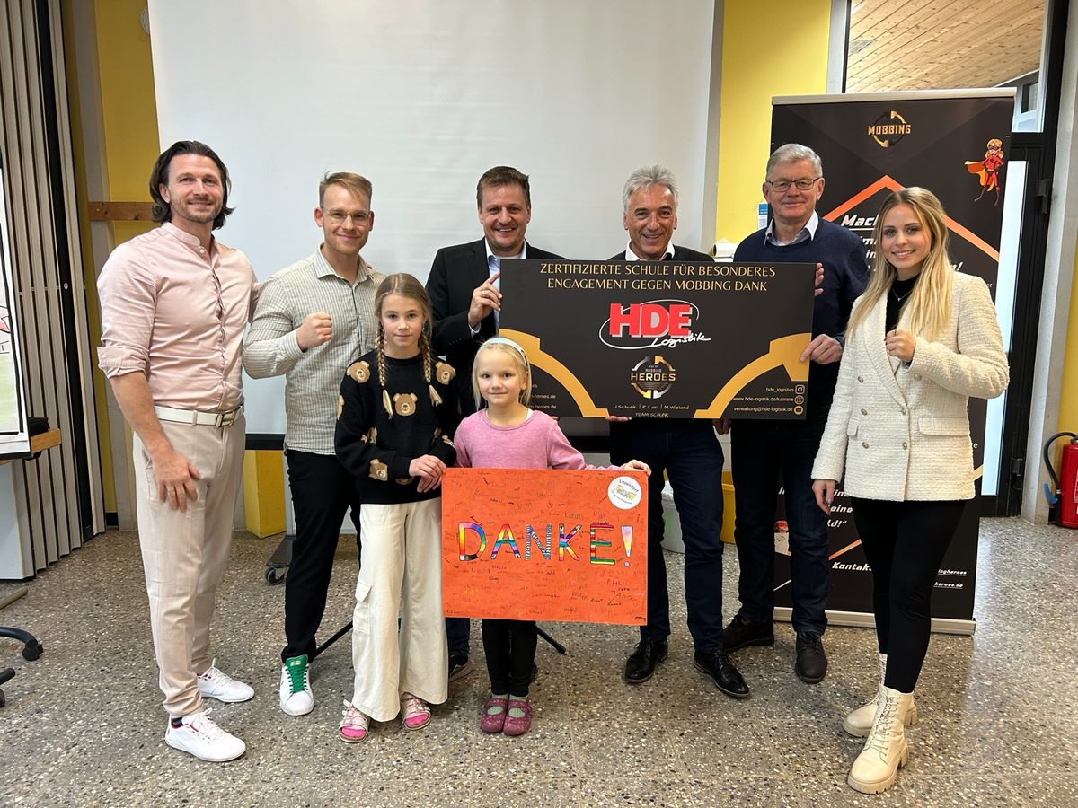 Übergabe der HDE-Logistik-Patenschaft: zwei Schülerinnen halten ein selbst gestaltetes DANKE-Plakat, dahinter Vertreter von HDE Logistik und das EOM-Team
