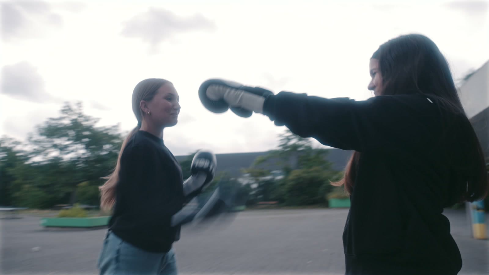 Zwei Schülerinnen üben auf dem Schulhof, eine schlägt mit Boxhandschuhen auf die Pratzen der anderen
